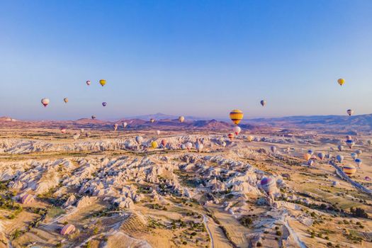 Colorful hot air balloons flying over at fairy chimneys valley in Nevsehir, Goreme, Cappadocia Turkey. Spectacular panoramic drone view of the underground city and ballooning tourism. High quality.