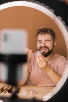 Man talking on cosmetics holding a makeup tools while recording his video. Guy making video for his blog on cosmetic product.