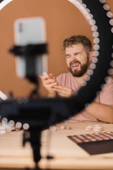 Man talking on cosmetics holding a makeup tools while recording his video. Guy making video for his blog on cosmetic product.