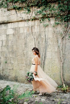 Bride with a bouquet walks past the medieval stone wall of the fortress. High quality photo