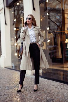 Stylish european woman in sunglasses is talking phone on city street background. High quality photo