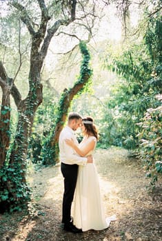 Groom hugs bride with his forehead against her forehead in the park. High quality photo