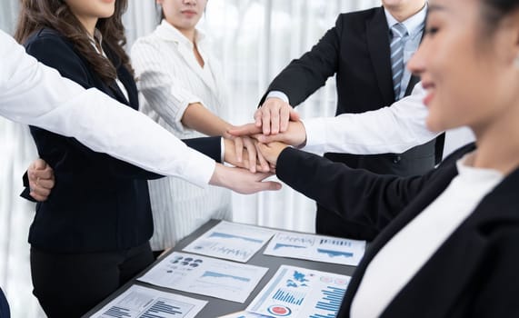 Closeup business team of suit-clad businessmen and women join hand stack together and form circle. Colleague collaborate and work together to promote harmony and teamwork concept in office workplace.