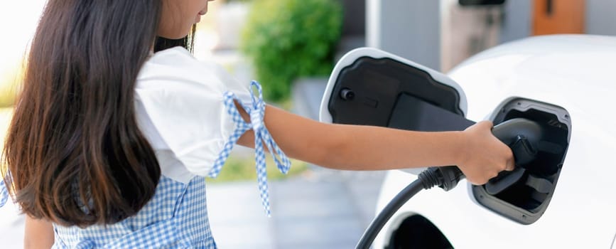 A playful girl holding an EV plug, a home charging station providing a sustainable power source for electric vehicles. Alternative energy for progressive lifestyle.