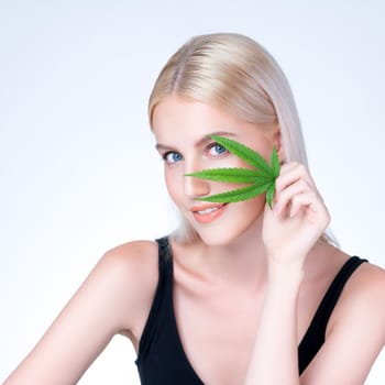 Personable beautiful white blond hair with perfect smooth makeup skin hold cannabis green hemp in isolated background for natural CBD skincare treatment with expressive facial and gesture expression.