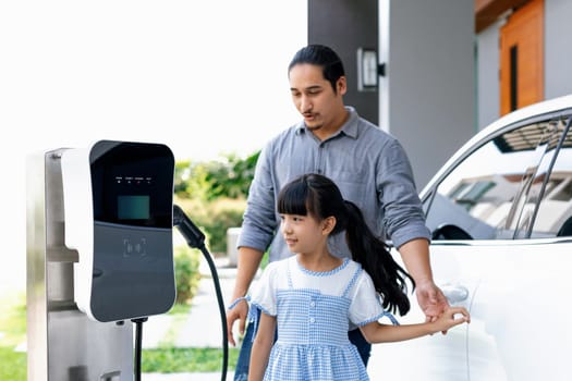 Progressive concept of a father and daughter who have just returned from school in an electric vehicle that is being charged at home. Electric vehicle driven by renewable clean energy.