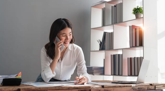 Beautiful Asian businesswoman is using smartphone to chat with customers at work and play various social media applications in a relaxed smile