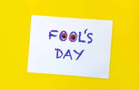 Text word Fool's day on sheet of paper with funny eyes and. 1 april message handwritting on sheet of paper. Bright yellow background. International humor day.