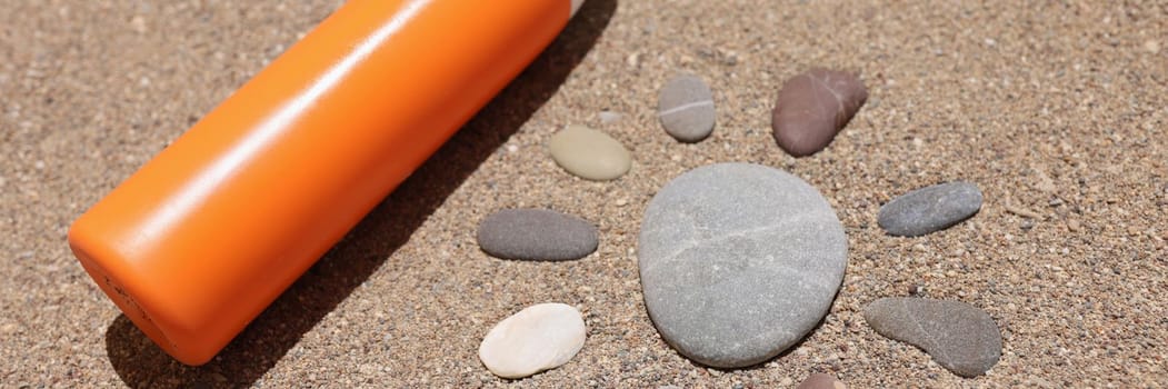 Sun made of stones on sea sand orange liquid bottle of cream or lotion. Sun protection and sunscreen lotion or spray spf