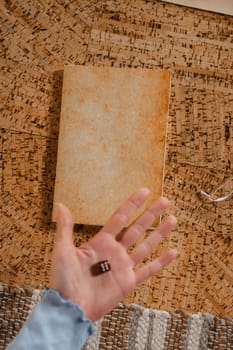 There is a dice in a person's hand. Close-up of a hand with a dice on the background of a notebook.