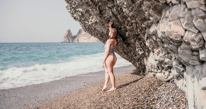 Beach vacation. Hot beautiful woman in sunhat and bikini standing with her arms raised to her head enjoying looking view of beach ocean on hot summer day.