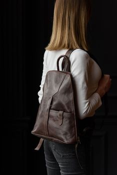 a blond girl in a white shirt poses while standing with a brown leather backpack on her back