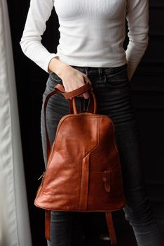 a blond girl in a white shirt poses while standing with a orange leather backpack in her hands