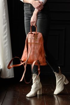 a blond girl in a white shirt poses while standing with a orange leather backpack in her hands