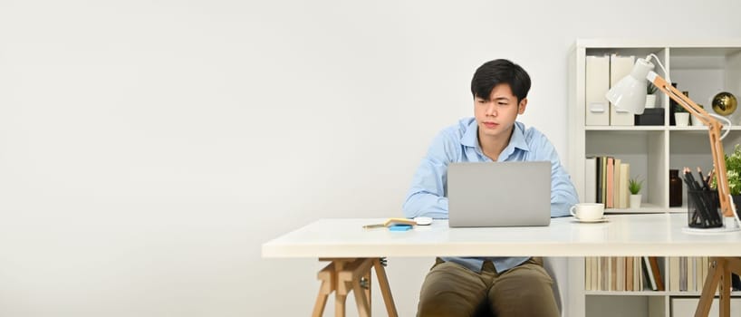 Handsome asian businessman sitting at working desk and using laptop computer. Horizontal banner, copy space for text.