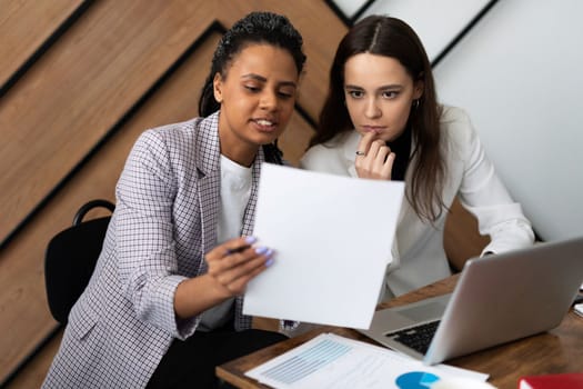 Business women at work discussing business with a laptop and documents in their hands.