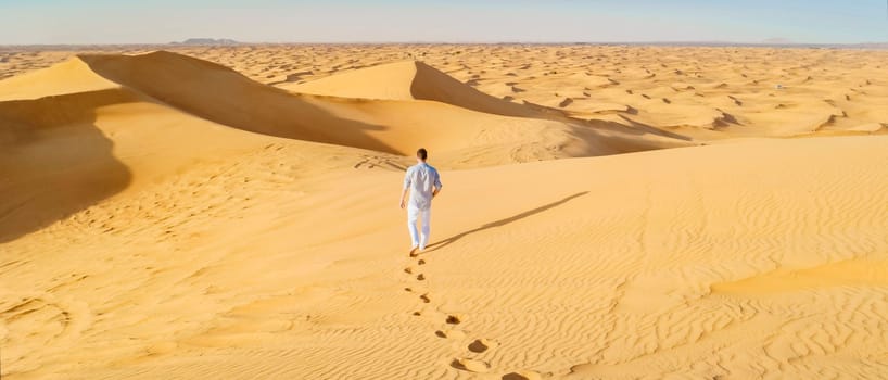 Young men walking in the desert of Dubai, Sand dunes of Dubai United Arab Emirates, sand desert on a sunny day in Dubai.