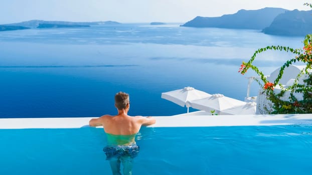 man relaxing in infinity swimming pool during vacation at Santorini, swimming pool looking out over the Caldera ocean of Santorini, Oia Greece, Greek Island Aegean Cyclades luxury vacation.