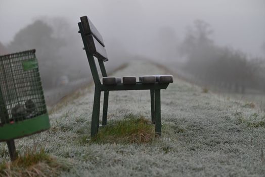 Park bench and a dustbin on a dike on a foggy morning in Wintertime