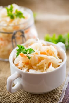 Sauerkraut with carrots and spices in a bowl on a wooden table.