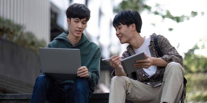 Two young Asian male college students discussing and working on their school project together.