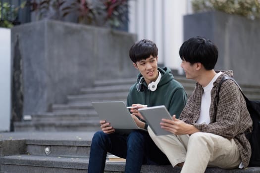 Two young Asian male college students discussing and working on their school project together.