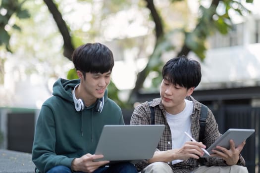 Two young Asian male college students discussing and working on their school project together.