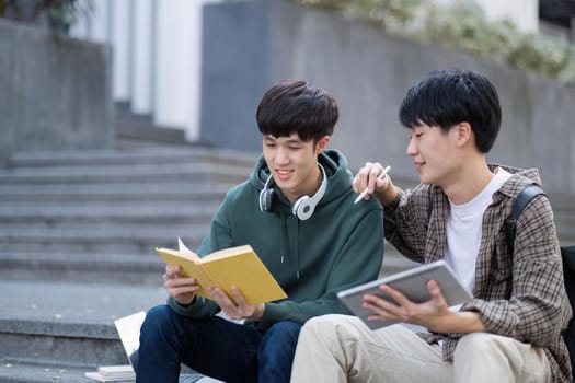 Two young Asian male college students discussing and working on their school project together.