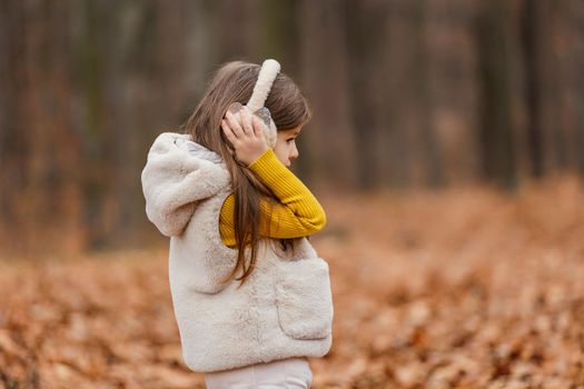 little girl in headphones walks through the autumn forest