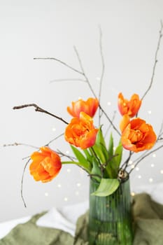 A very beautiful spring bouquet in a green vase stands on a table on a linen tablecloth, orange peony tulips