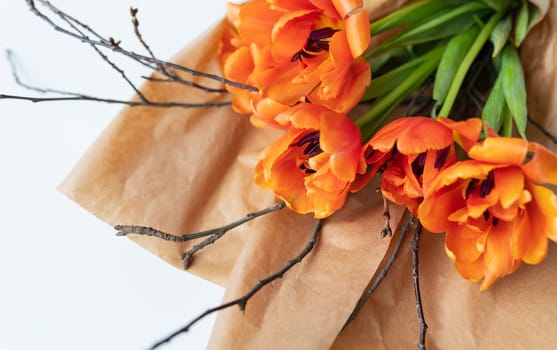 A very beautiful spring bouquet of orange peony tulips, along with branches of young cherries, lies in craft paper on a white table