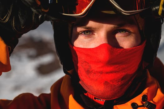 A young man looks directly into the camera, close-up of the eyes. Hands holding ski mask or goggles, expressive look.