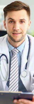 Portrait of a smiling handsome doctor working in clinic. Doctor cardiologist therapist choosing right method of treatment and medical diagnosis sitting at table with patient card