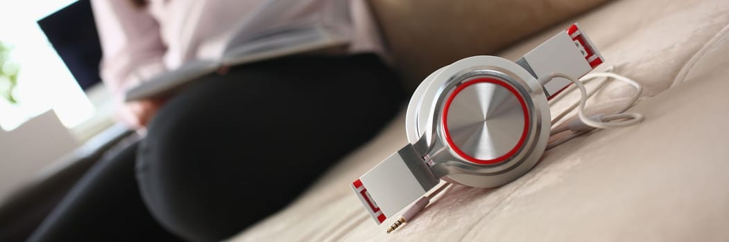 Fashionable white red headphones lie on the sofa in background person sits. Headphones and headsets for home