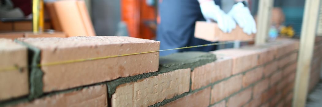 Professional builder lays bricks and builds a wall in apartment. Detail of manual adjustment of bricks concept