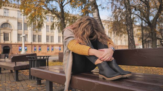 A young girl crying on a park bench in the fall