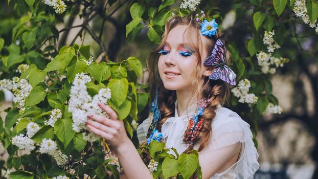 A young girl poses in white lilac with a beautiful hairstyle of flowers and butterflies