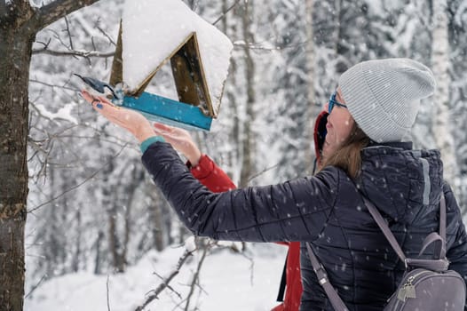 Woman in winter jacket feeding birds in snowy winter forest, snowy winter day.