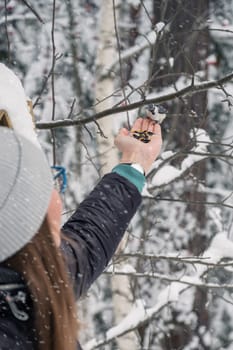 Woman in winter jacket feeding birds in snowy winter forest, snowy winter day.