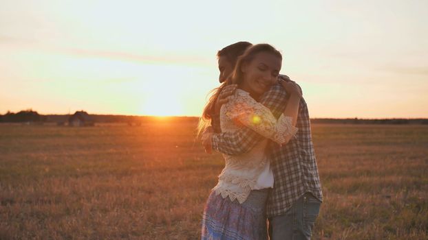 A guy is circling his girlfriend in his arms on a sunset background