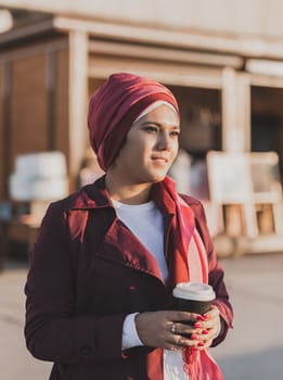 Modern arab girl in hijab walking by street and drinking coffee take away in spring time morning copy space