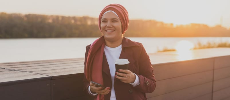 Asian muslim woman wearing hijab scrolling social networks having coffee break outdoor on city