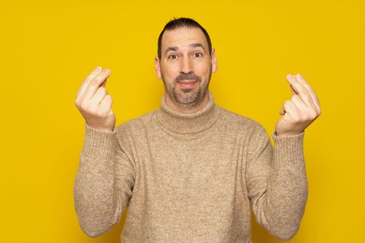 Handsome man about 40 years old wearing beige turtleneck sweater isolated over yellow background, doing italian gesture with hand and fingers confident expression