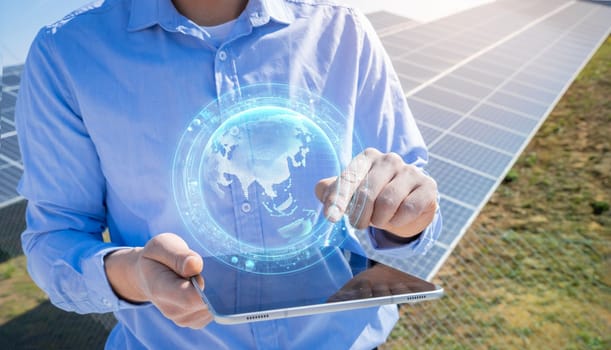 Unrecognizable engineer with a tablet with earth HUD hologram with photovoltaic solar panels system plant in the background. Green clean alternative energy concept.
