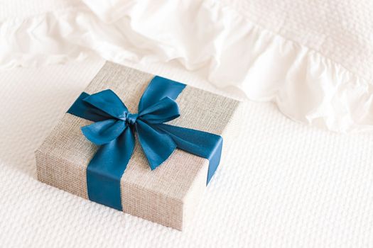 Holiday present and luxury online shopping delivery, wrapped linen gift box with blue ribbon on bed in bedroom, chic countryside style, close-up