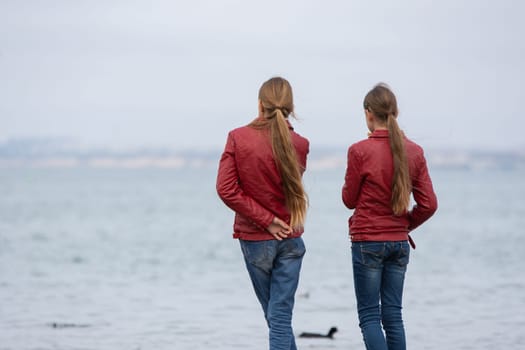 Two girls in identical clothes look at the sea, close- up, view from the back