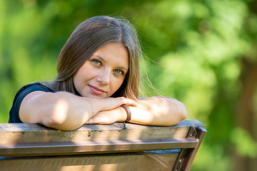 Portrait of a beautiful girl sitting on a bench and looking happily into the frame a