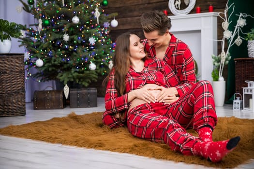 A couple cuddles on a fluffy carpet. The woman lies leaning with her back against the man. The woman is advanced in pregnancy and exposes her naked pregnant belly. Both are smiling.