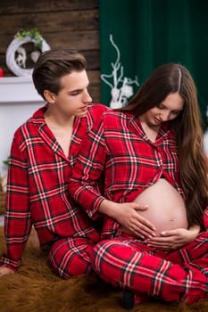 A man and a woman sit on a brown fluffy carpet. The man sits behind the woman, while the woman exposes her pregnant belly by exposing it.