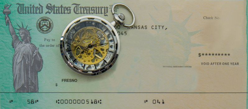 Photo of blank US Treasury check mock up with a modern pocket watch on top. Treasury check has statue of liberty image. Pocket watch has transparent case showing gears, springs inside. High quality photo